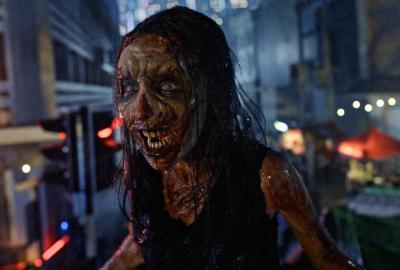 A ghostly woman with a blood-streaked face stands in a dark nighttime setting.